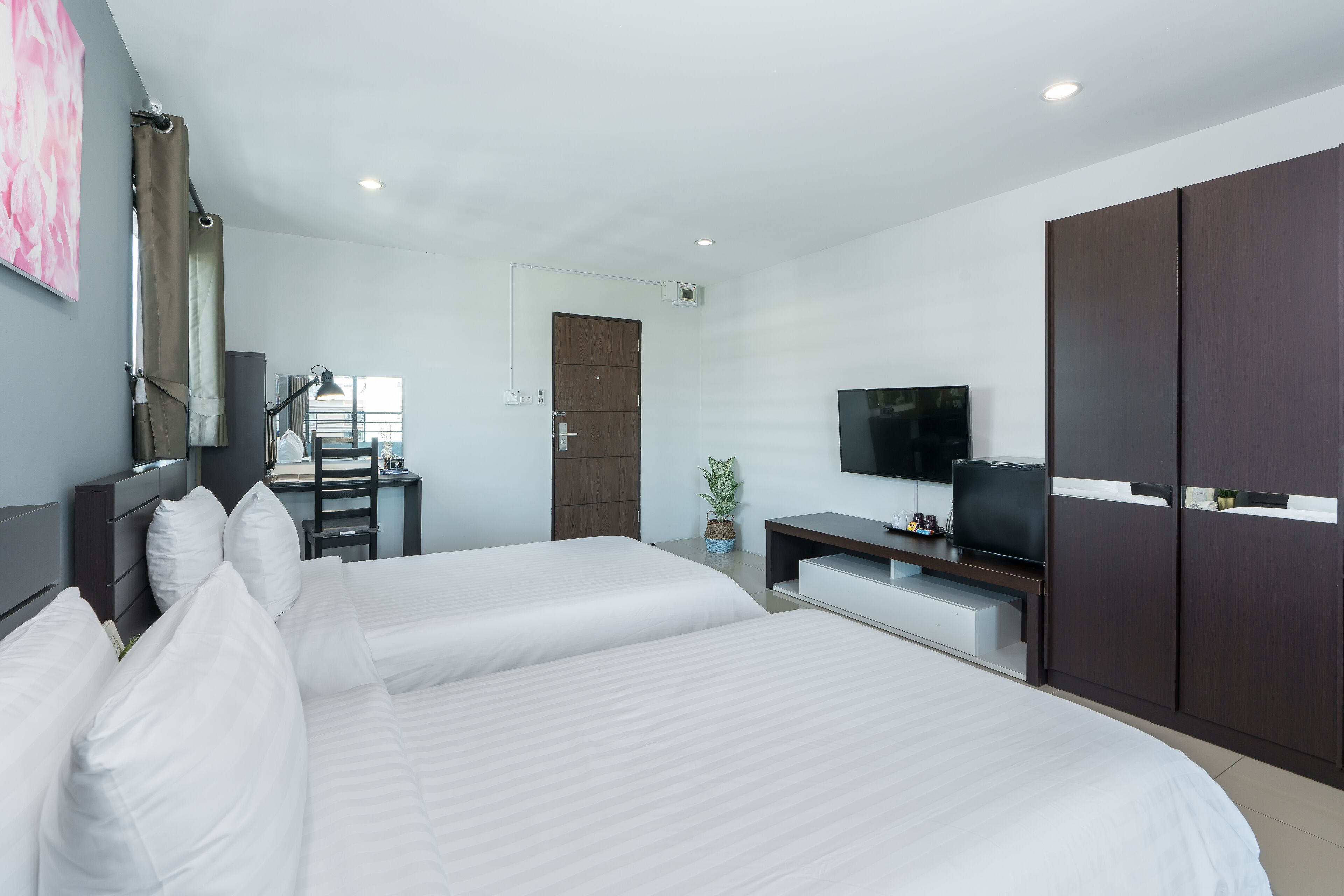 A hotel room with two beds, a TV, a desk with a chair, and a wardrobe.