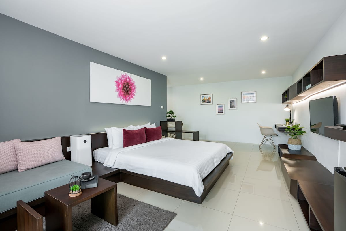 Quarto moderno com cama, sofá, mesas de cabeceira e televisão.