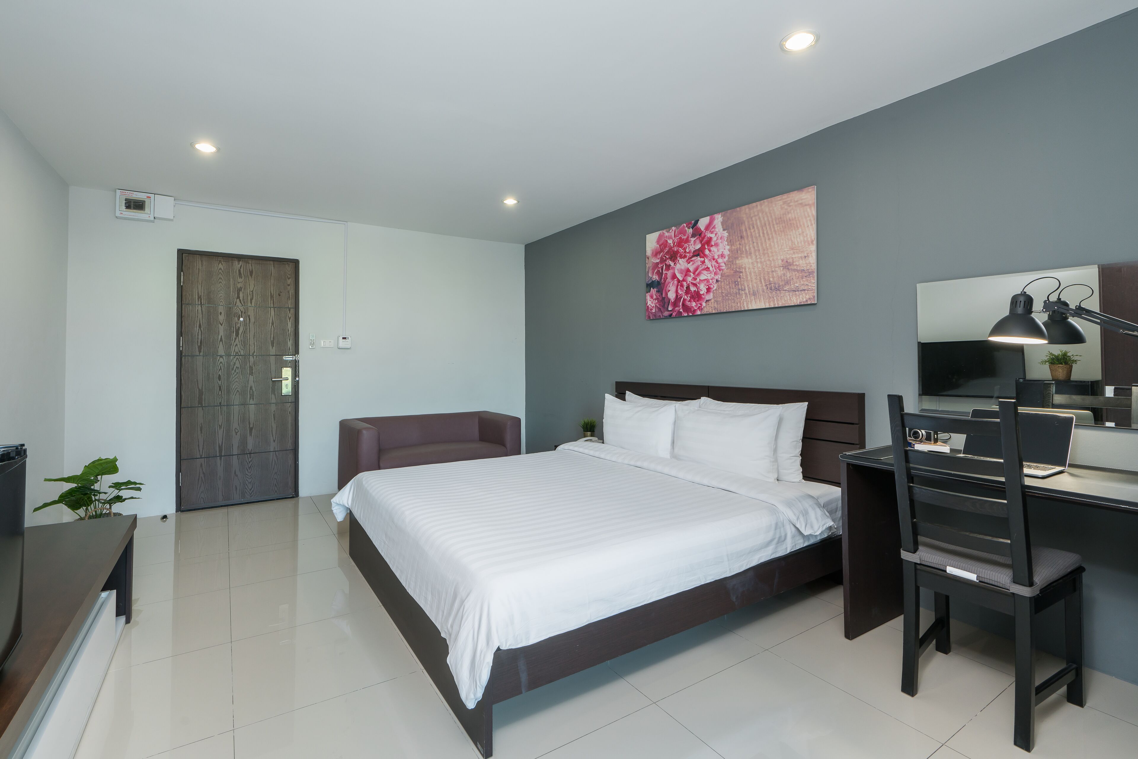 Un dormitorio moderno con una cama grande, un escritorio con una silla, una lámpara de escritorio y un televisor montado en la pared.