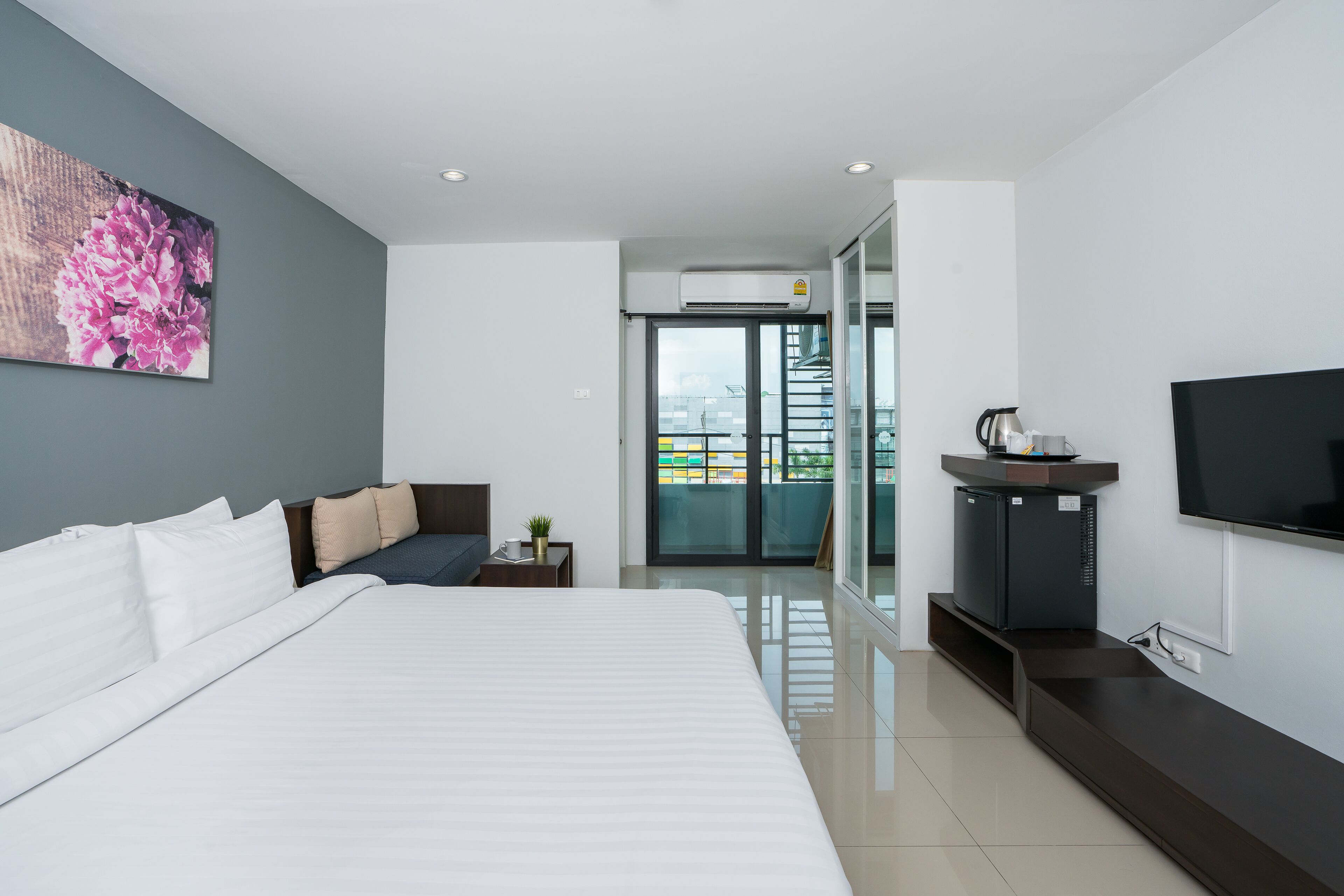 Quarto de hotel moderno com uma cama grande, televisão de tela plana, pequeno espaço de cozinha e varanda com vista.