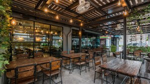 Un café en plein air avec des tables et des chaises en bois, de grandes fenêtres et des guirlandes lumineuses.
