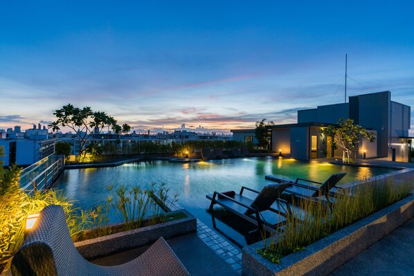 A rooftop pool with lounge chairs and a cityscape view at dusk.