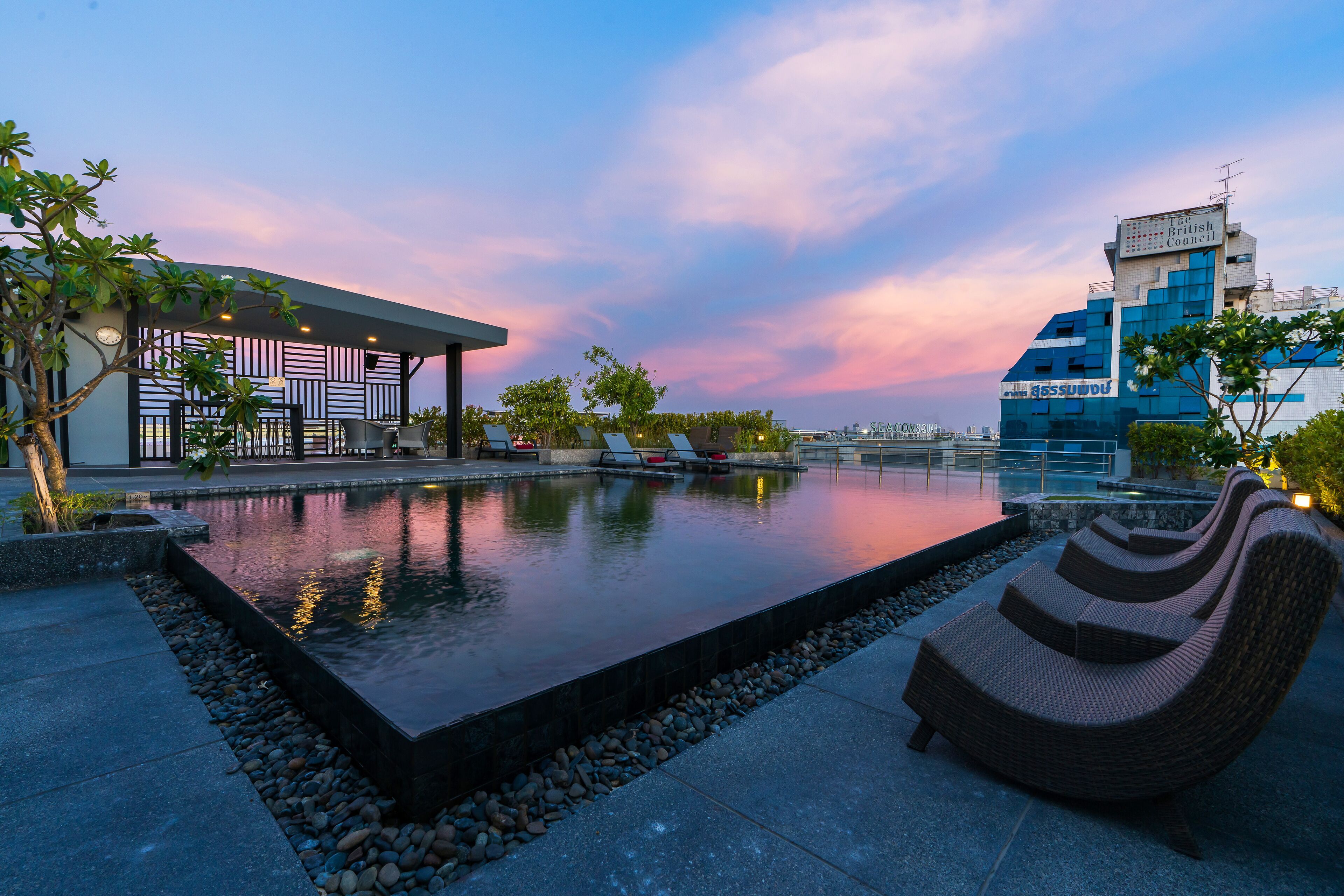 A modern outdoor pool area with lounge chairs, a building with a geometric facade, and a clear view of the sky.