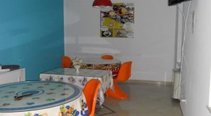 Ein Essbereich mit einem runden Tisch und orangefarbenen Stühlen, einem Poster an der Wand und einer roten Lampe.