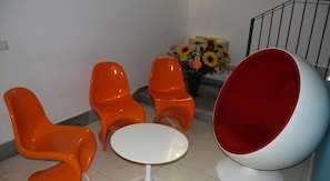 Ein modernes Zimmer mit orangefarbenen Stühlen, einem weißen Tisch und einem großen, rot-weißen Sitzball.
