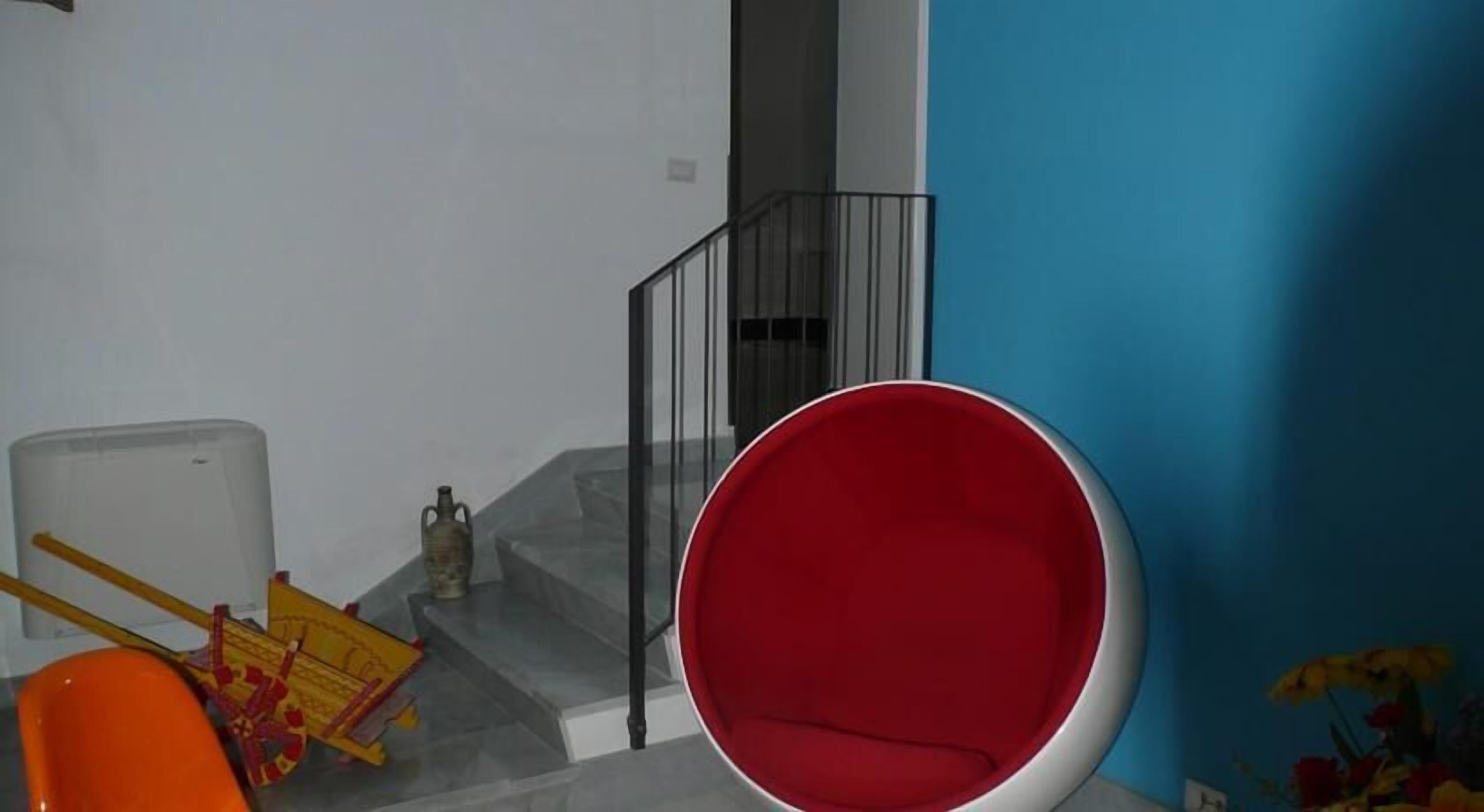 Uma escadaria com guarda-corpo de vidro, uma cadeira vermelha e uma pequena mesa com um vaso de flores.