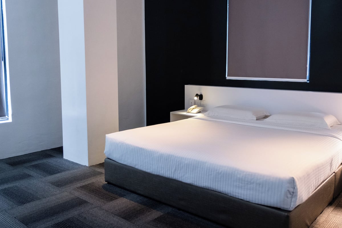 Ein modernes Hotelzimmer mit einem großen Bett, einem Nachttisch mit einer Lampe und einem Fenster.