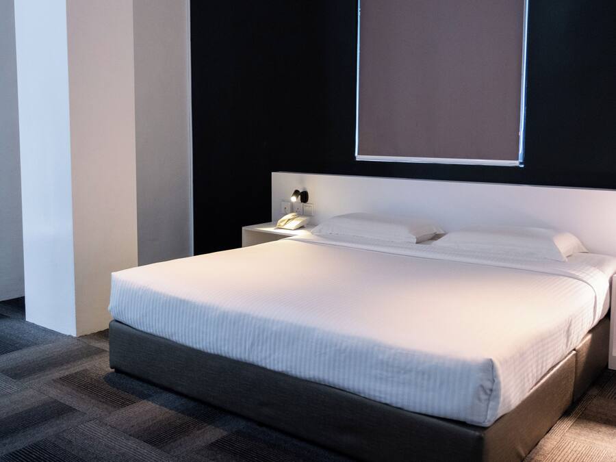 A modern hotel room with a large bed, a bedside table with a lamp, and a window.