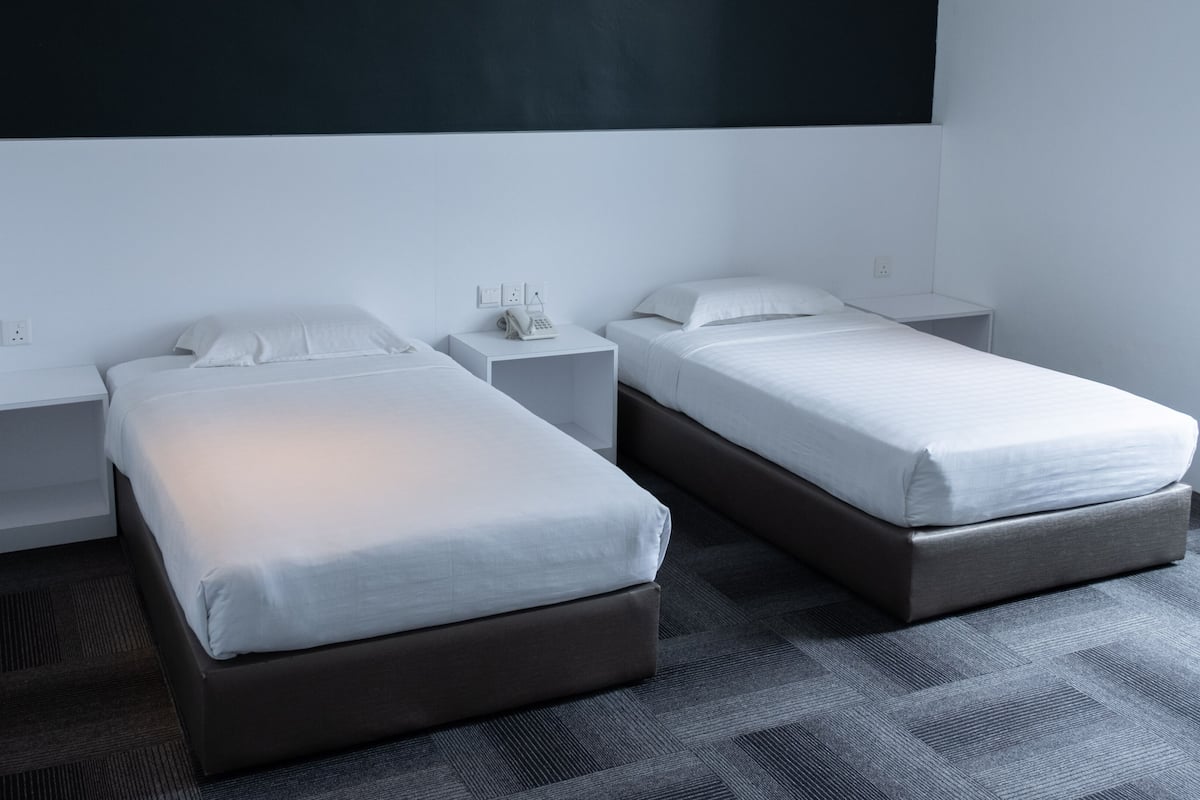 Ein modernes Hotelzimmer mit zwei Einzelbetten, einer großen, dunklen Wand und einem gemusterten Teppich.