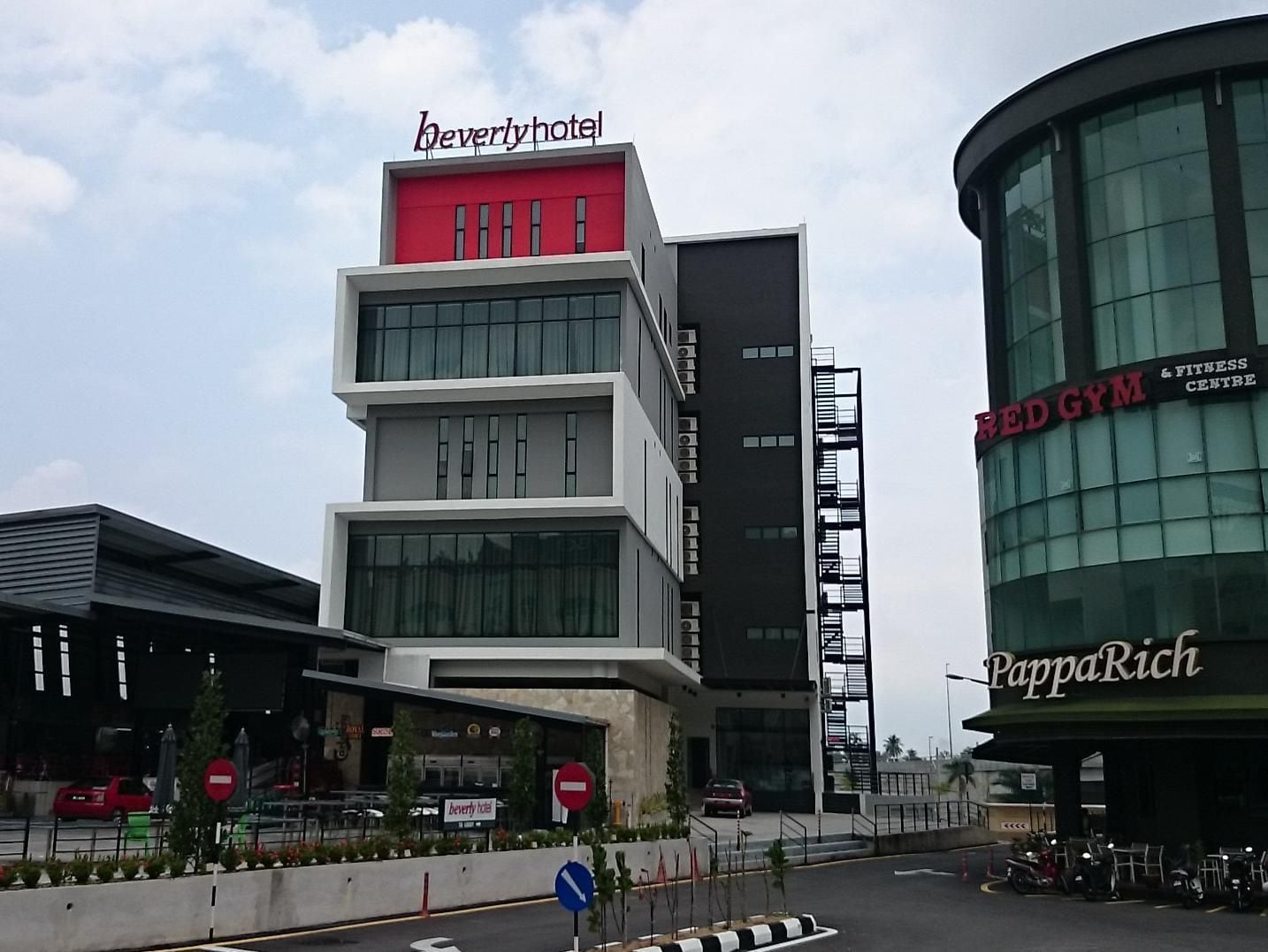 A multi-story hotel with a red and white facade, a fitness center, and a restaurant named PappaRich.