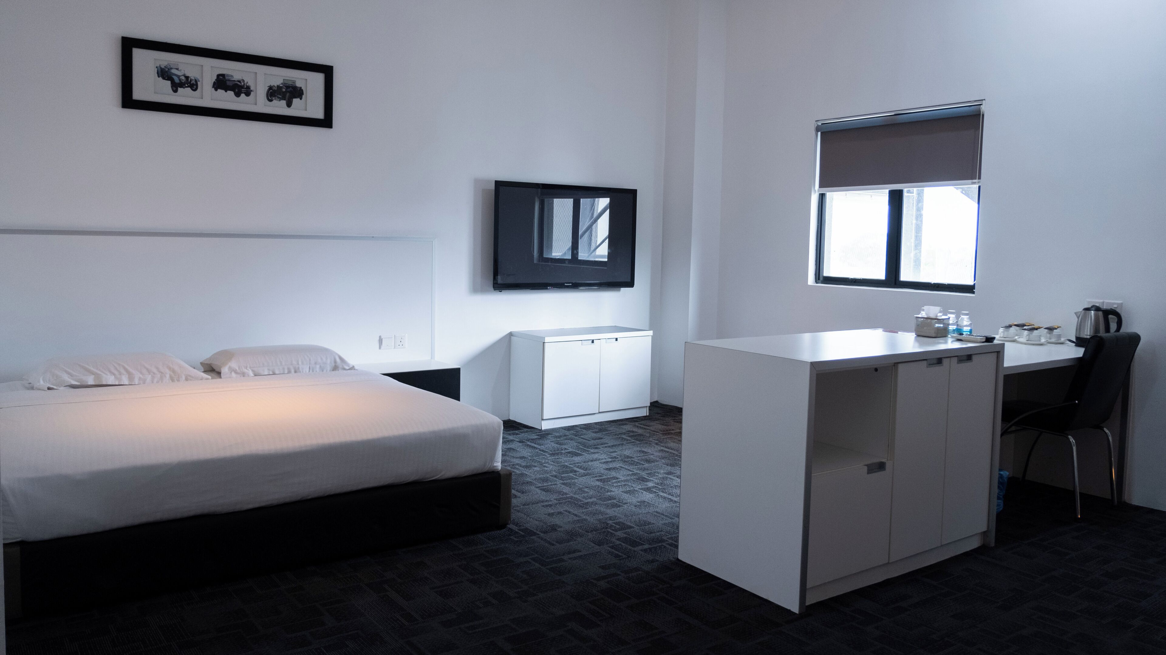 Habitació d'hotel amb llit, escriptori, cadira, radiador i finestra.