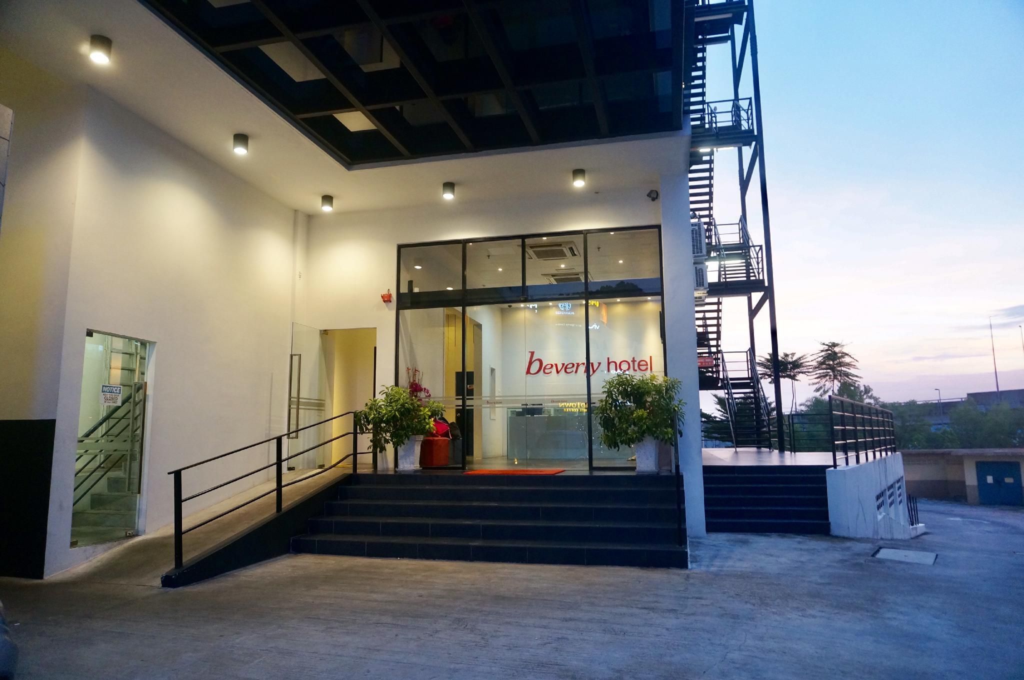 The entrance to the Beverly Hotel with a staircase leading up to the entrance, a glass facade, and a clear sky in the background.