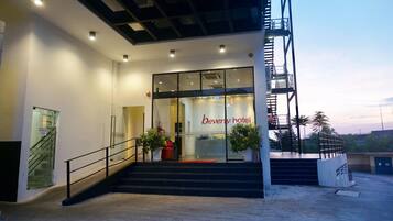 The entrance to the Beverly Hotel with a staircase leading up to the entrance, a glass facade, and a clear sky in the background.