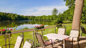An outdoor seating area with a table and chairs overlooking a lake, surrounded by greenery and trees. - Emsland Hotel Saller See (Freren)