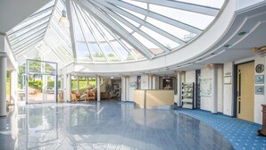A spacious lobby with a high ceiling and a glass roof, allowing natural light to fill the area. - Emsland Hotel Saller See (Freren)