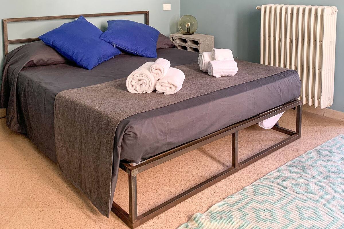 A bedroom with a bed, pillows, towels, a bedside table, a lamp, and wall decorations.