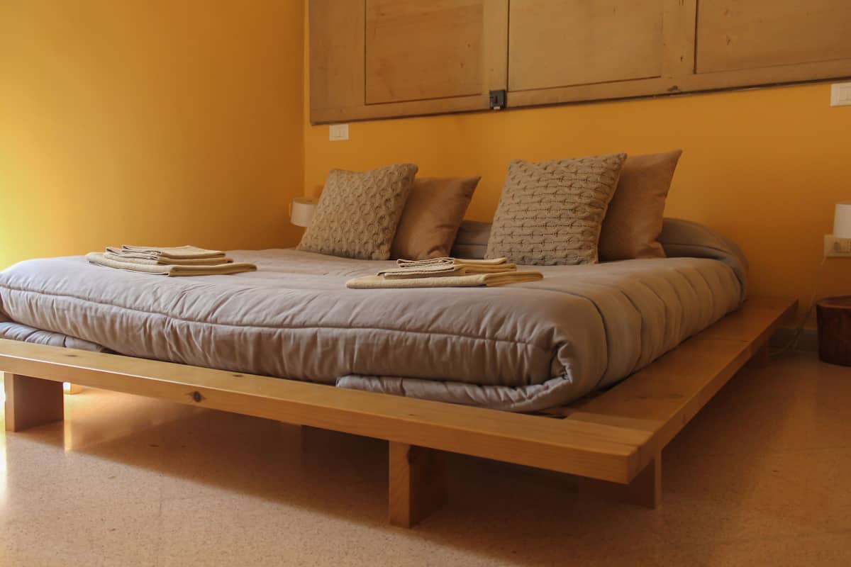 A bed with a wooden frame, a grey mattress, and multiple pillows.