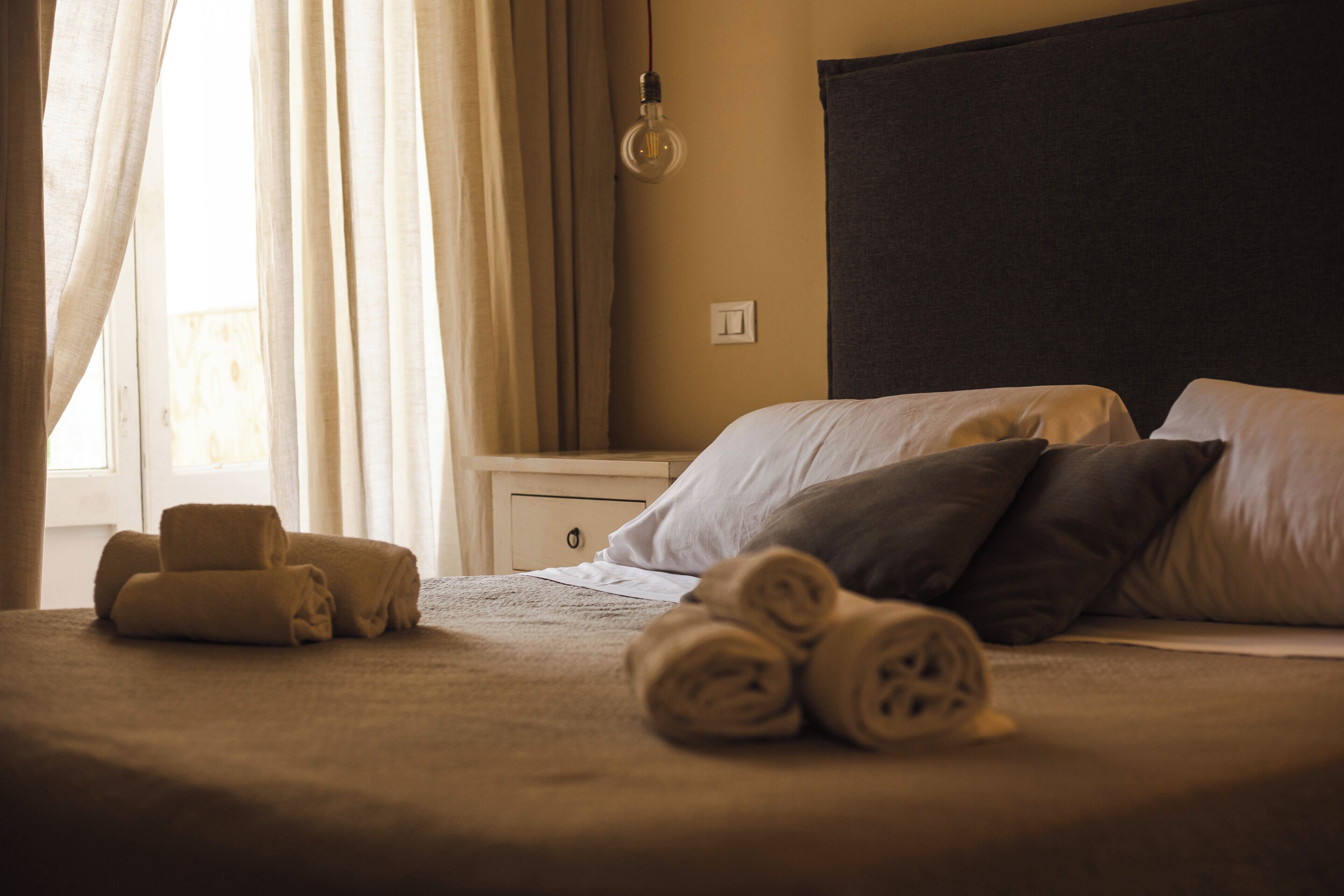 A neatly made bed with rolled towels, a bedside table, and a lamp.