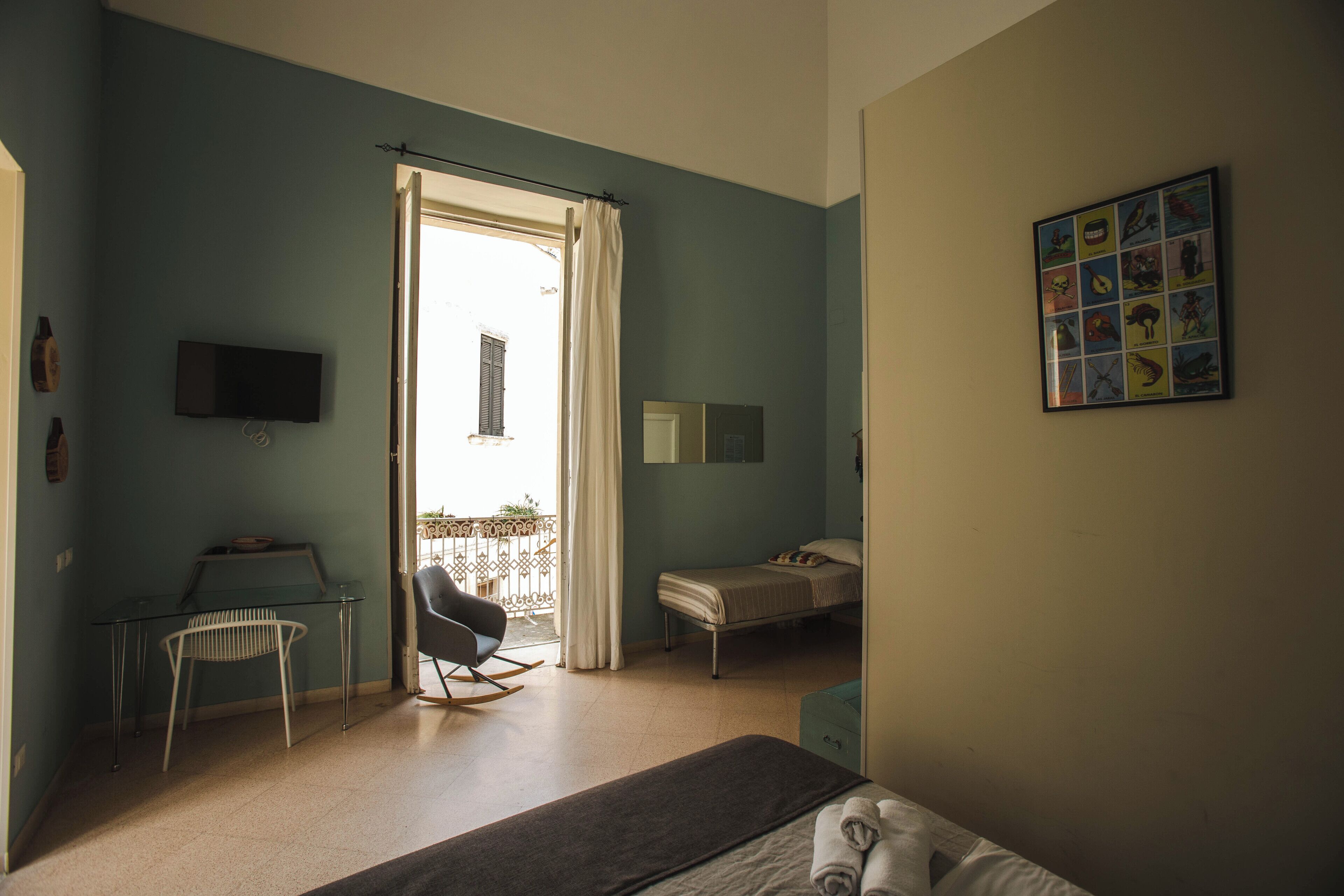 A room with a bed, a desk, a chair, a TV, and a balcony with a view.