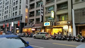 A street with parked motorcycles and a car, buildings with signage, and a storefront with a sign that reads "PEONY KOREA". - Long Siang Hotel (Kaohsiung)