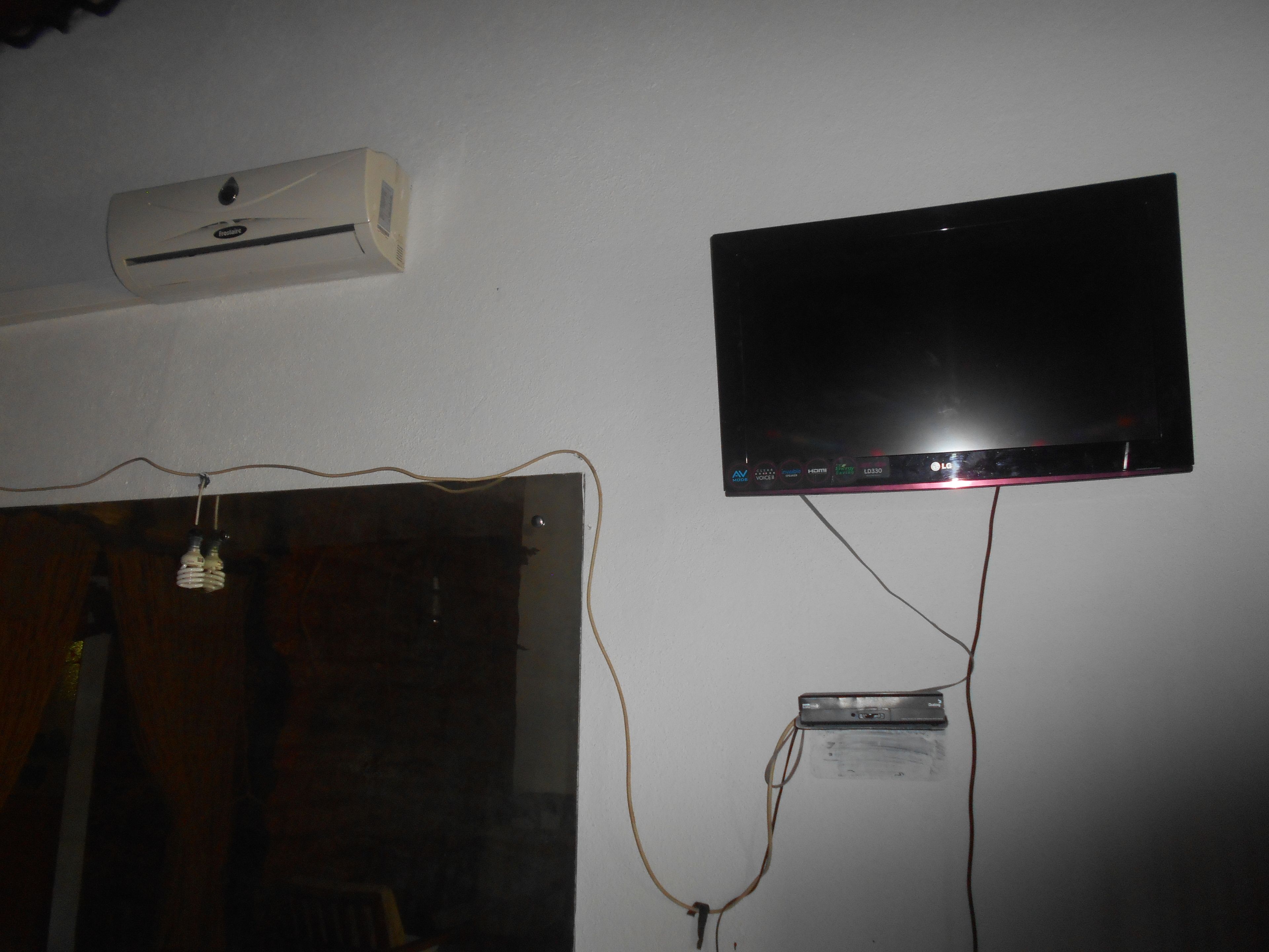 A wall-mounted television with visible HDMI and AV inputs, an air conditioning unit, and a power strip.