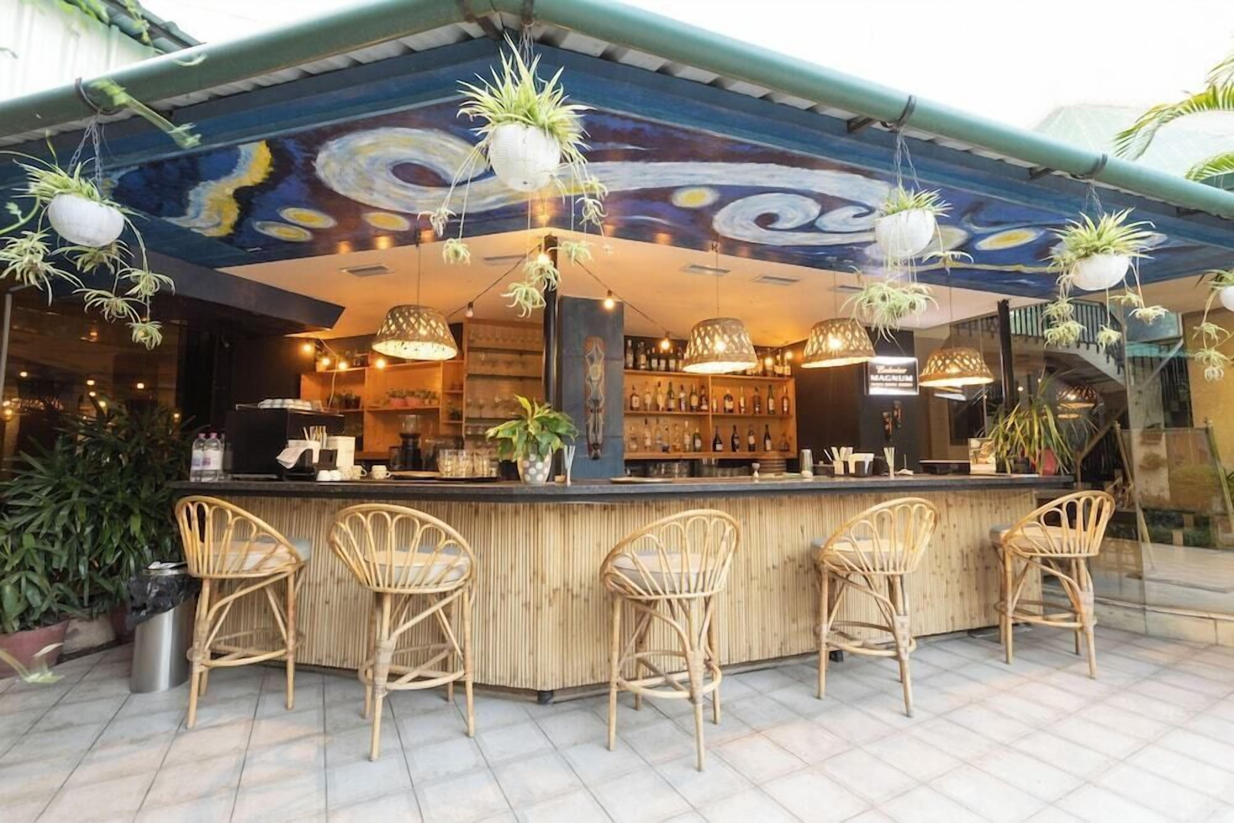 A bar area with a counter, wicker chairs, hanging plants, and a ceiling mural.