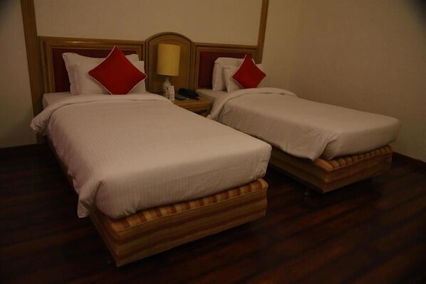 Dos camas individuales con cabeceros de madera y almohadas rojas, una mesita de noche con lámpara, y suelo de madera.