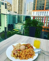 A dining table with a plate of food, a glass of orange juice, and a view of a cityscape with high-rise buildings.