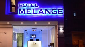 Ein moderner Hotel Eingang mit Glasfassade, einer Rezeption und einem blau beleuchteten Schild.