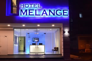 A modern hotel entrance with a glass facade, a reception desk, and a blue illuminated sign.