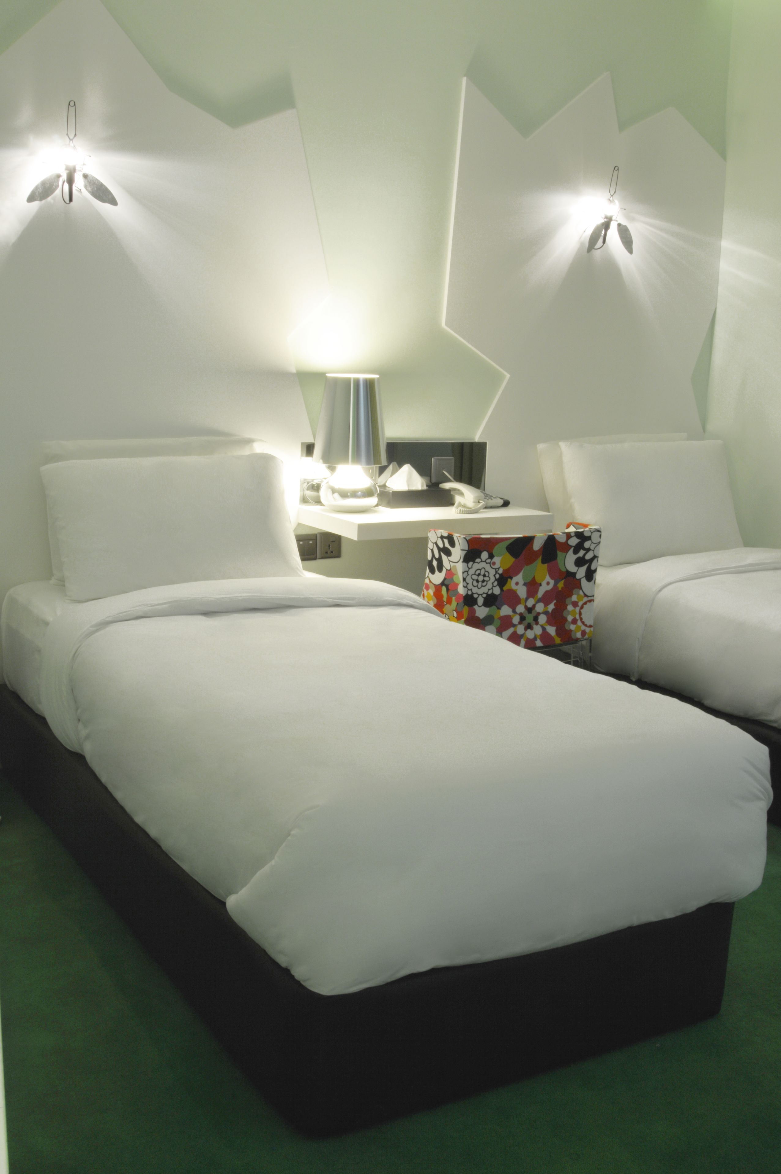 Ein Hotelzimmer mit zwei Betten, einem Schreibtisch mit Lampe und einem farbenfrohen Kissen.