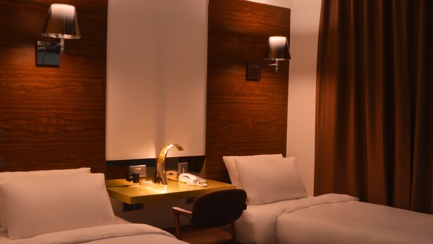 Ein Hotelzimmer mit zwei Betten, einem Schreibtisch mit Lampe, einem Telefon und einem Spiegel.