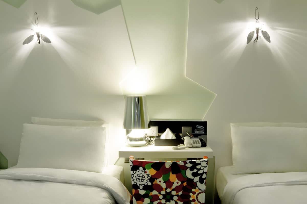 A hotel room with two beds, a desk with a lamp, a telephone, and a mirror.