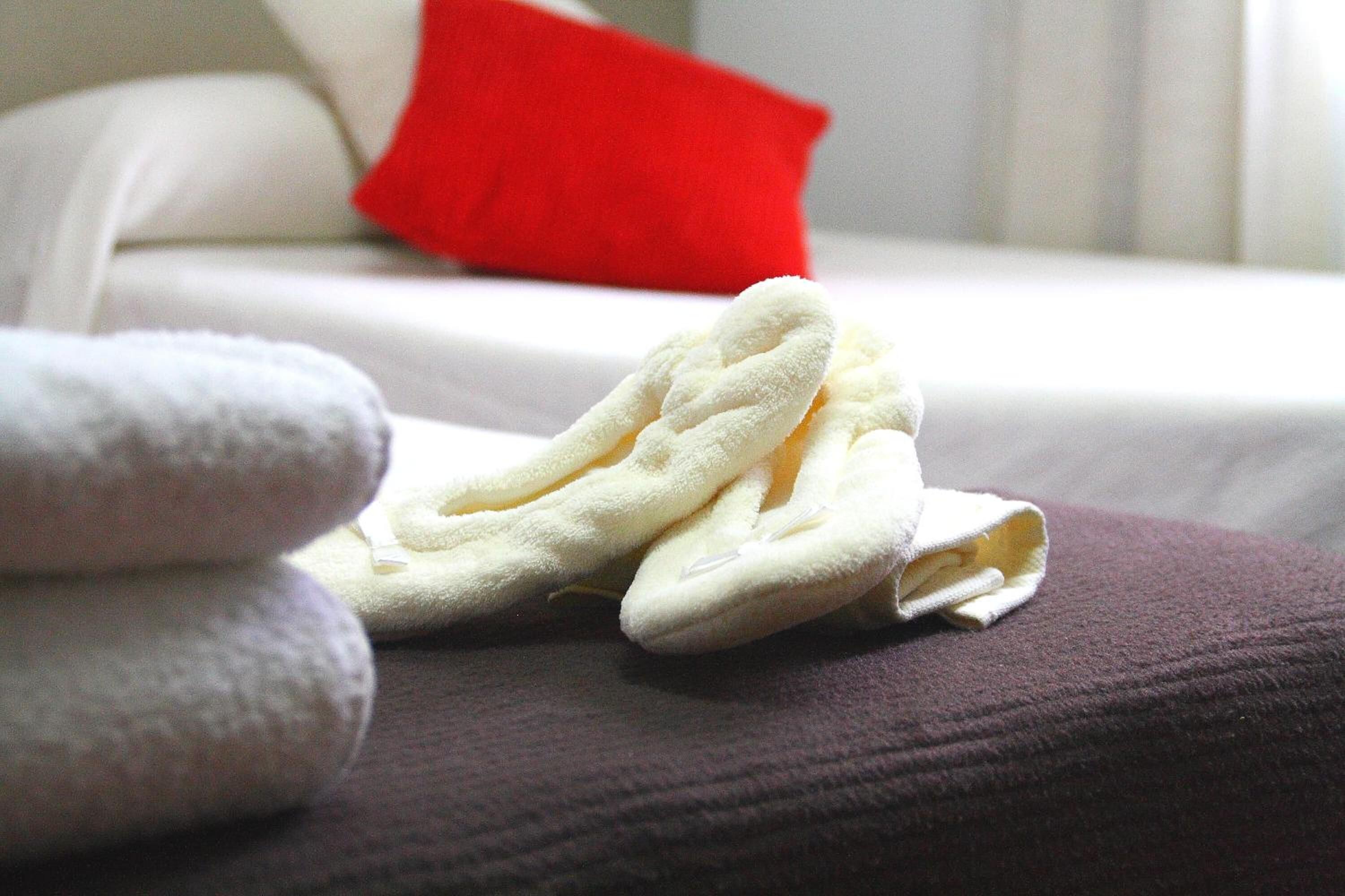Una cama bien tendida con una almohada roja y una pila de toallas blancas sobre un cubrecolchón morado.