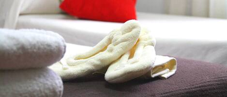 Cama bem arrumada com travesseiro vermelho e uma pilha de toalhas brancas sobre um cobreleiro roxo.