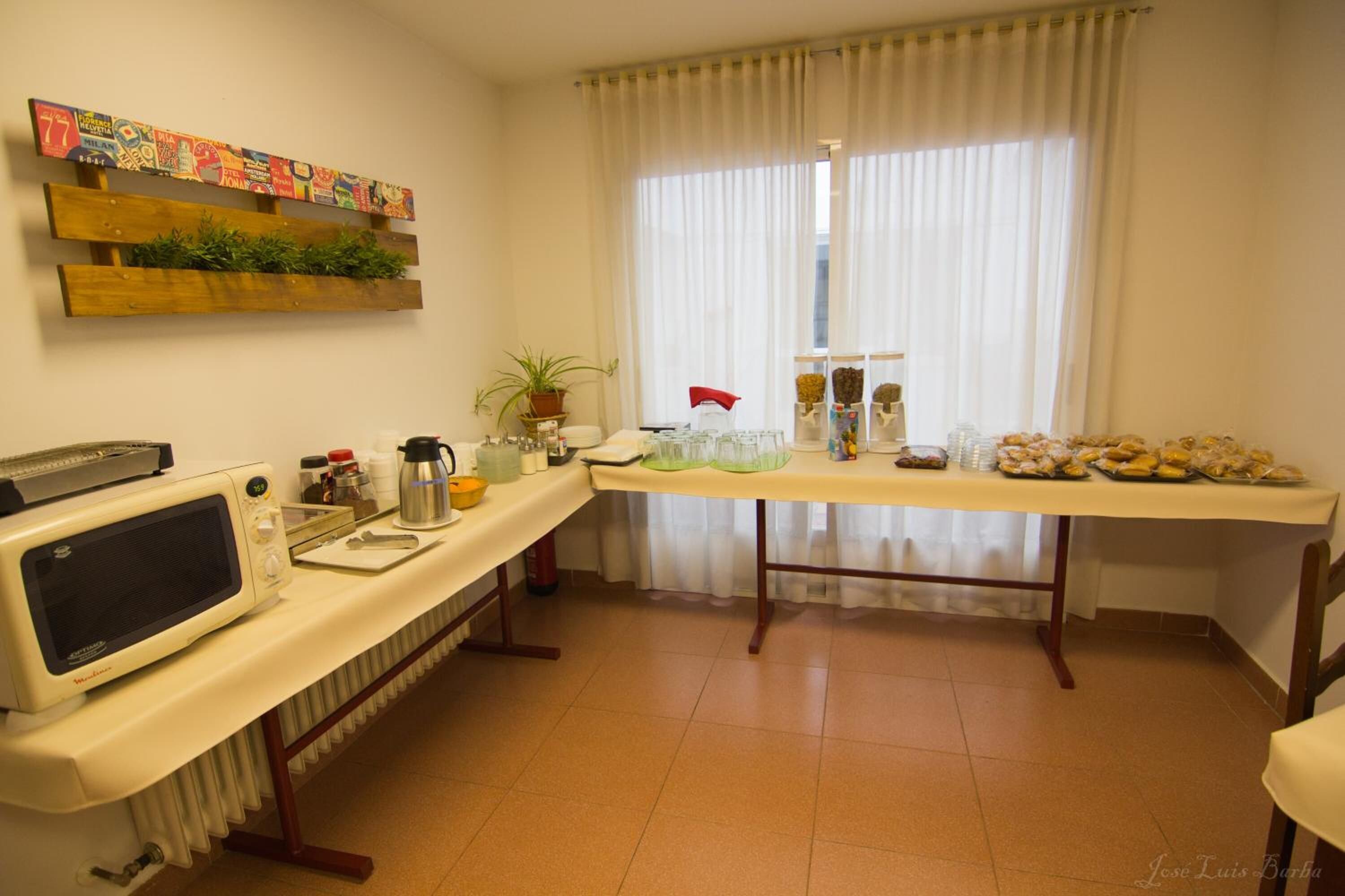 A kitchen with a microwave, a table with food items, a potted plant, and a window with curtains.