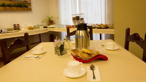 A breakfast table with a coffee pot, cups, a basket of pastries, and a vase of flowers.