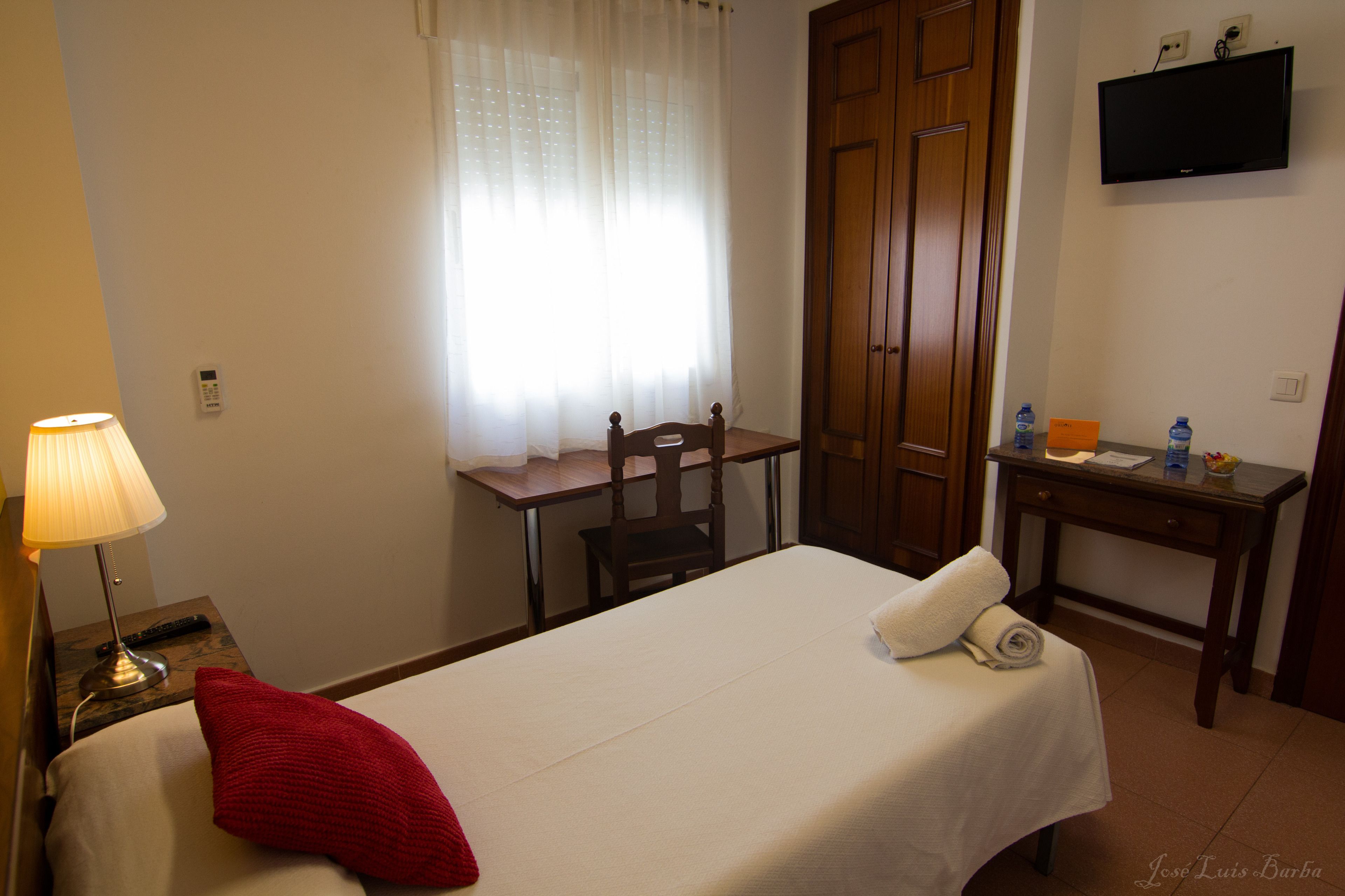 Una habitación de hotel con cama, escritorio, silla, televisión y ventana con cortinas.