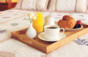 Una bandeja de desayuno con un croissant, frutos rojos, un vaso de zumo de naranja, un florero con una flor y una taza de café sobre la cama.
