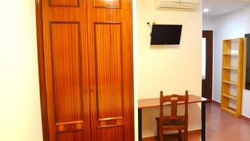 Uma porta de madeira, uma escrivaninha com uma cadeira, uma televisão e uma estante de livros num quarto.