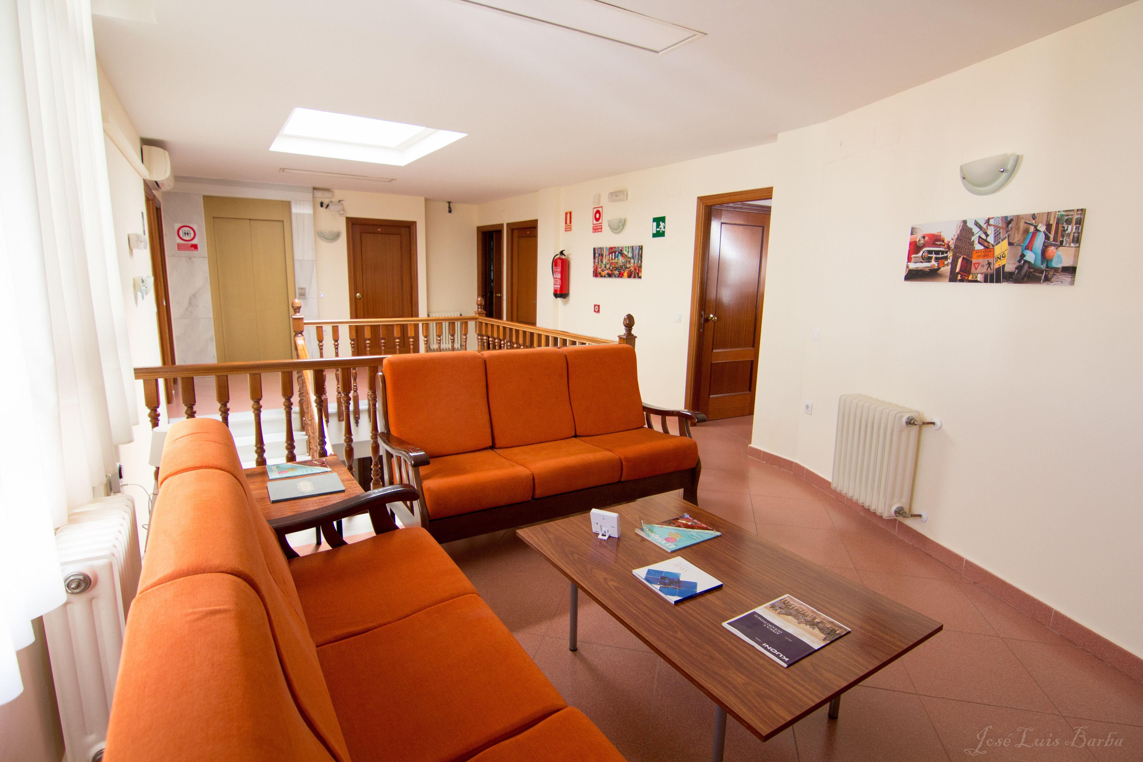 A hotel lobby with orange seating, a wooden coffee table, and a staircase leading to another floor.