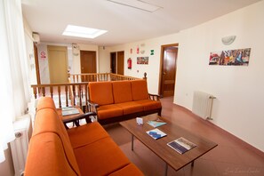 Un vestíbulo de hotel con asientos anaranjados, una mesa de centro de madera y una escalera que sube a otro piso.