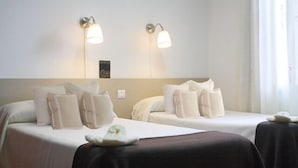 A hotel room with two beds, each with white linens and pillows, and two wall-mounted light fixtures.