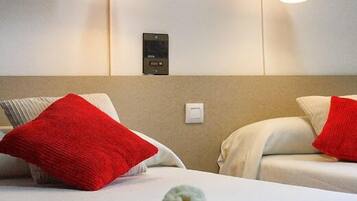 Habitación de hotel con dos camas, cada una con una almohada roja y una blanca. Hay luces fijadas a la pared sobre las camas.