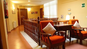 A hotel lobby with a wooden railing, orange upholstered chairs, a wooden table, and a fire extinguisher.