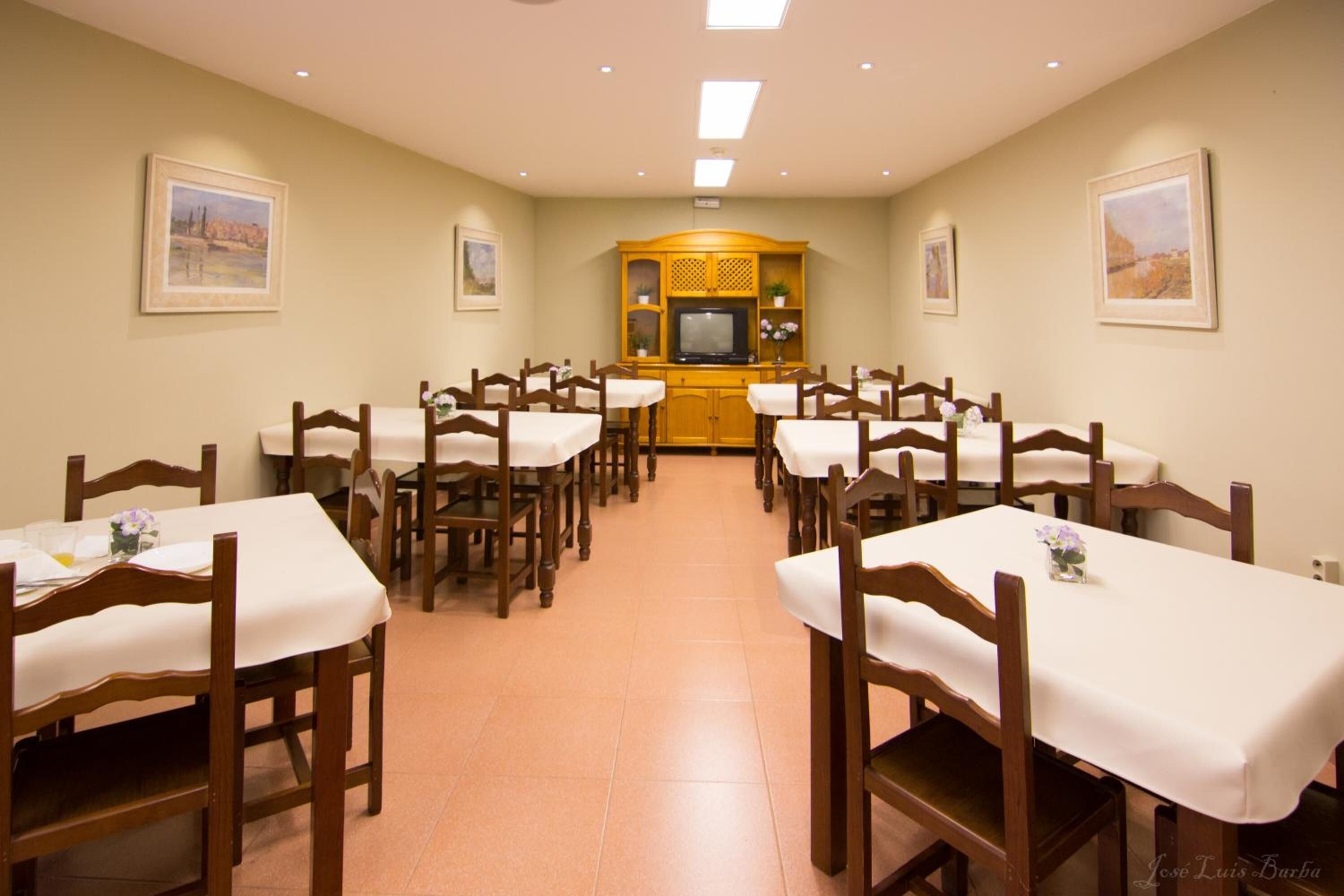Un comedor con varias mesas y sillas, un televisor y cuadros en las paredes.