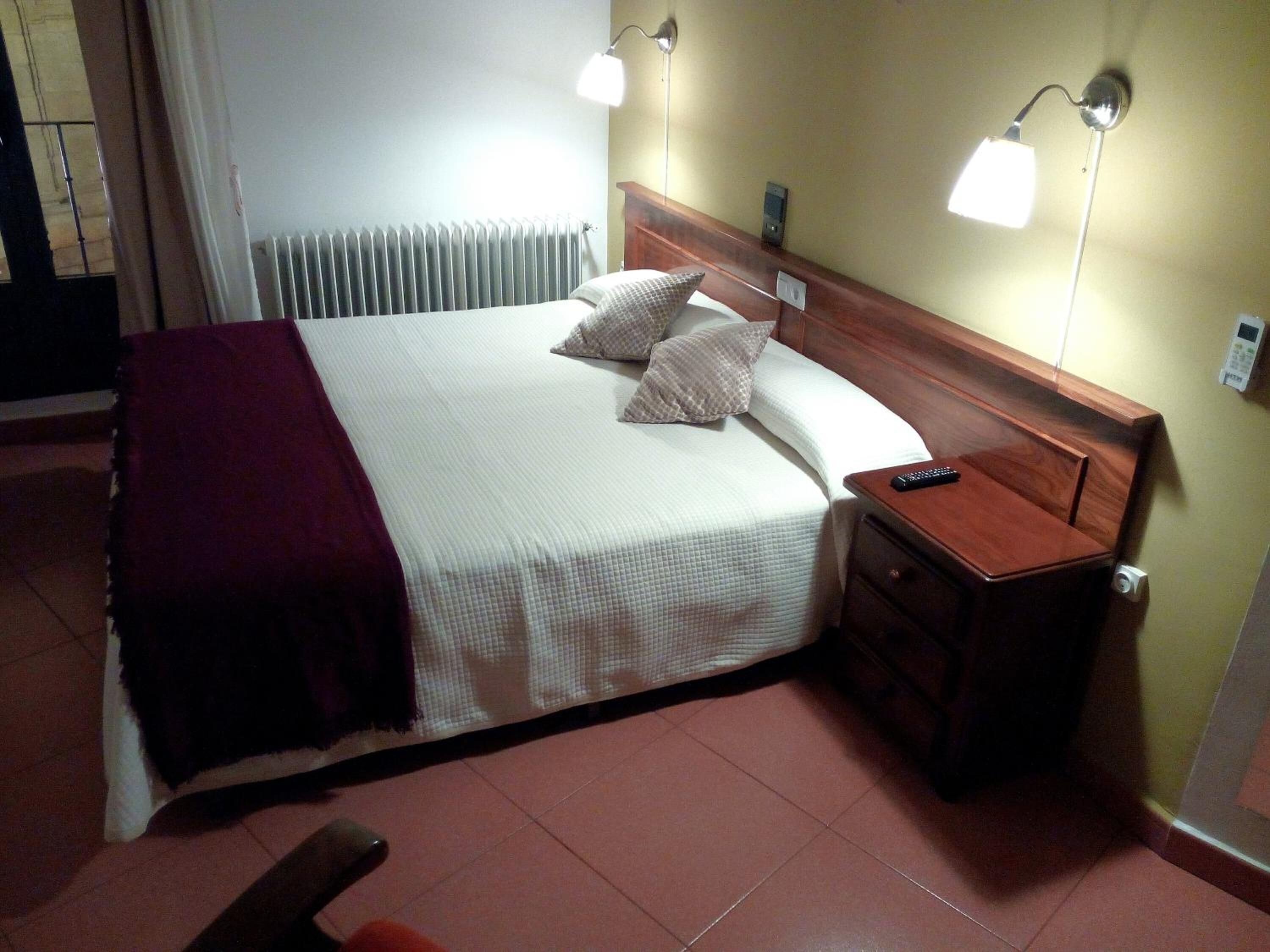 A hotel room with a bed, bedside lamps, a nightstand, and a remote control.