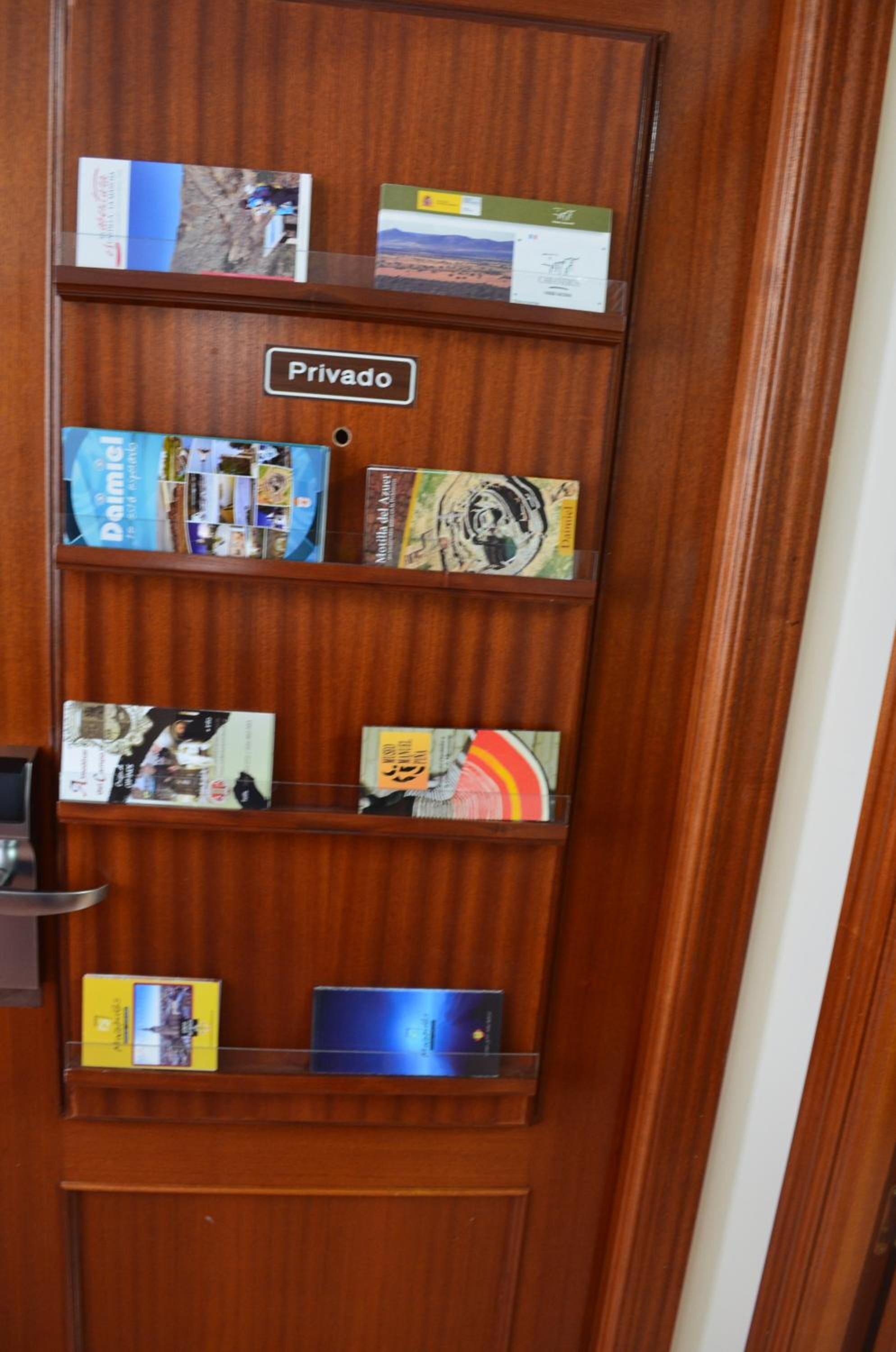 A wooden door with a 'Privado' sign and various travel brochures and a laptop on the shelves.