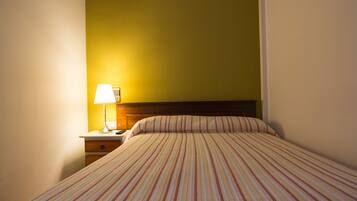 Habitación de hotel con cama, mesita de noche, lámpara y pared con un detalle amarillo.