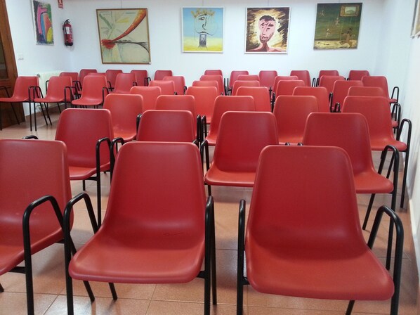 Una habitación con filas de sillas rojas y una pared blanca con pinturas.